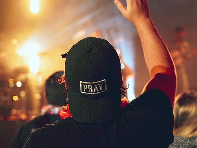 Person raising his hand in worship with a Pray baseball cap on