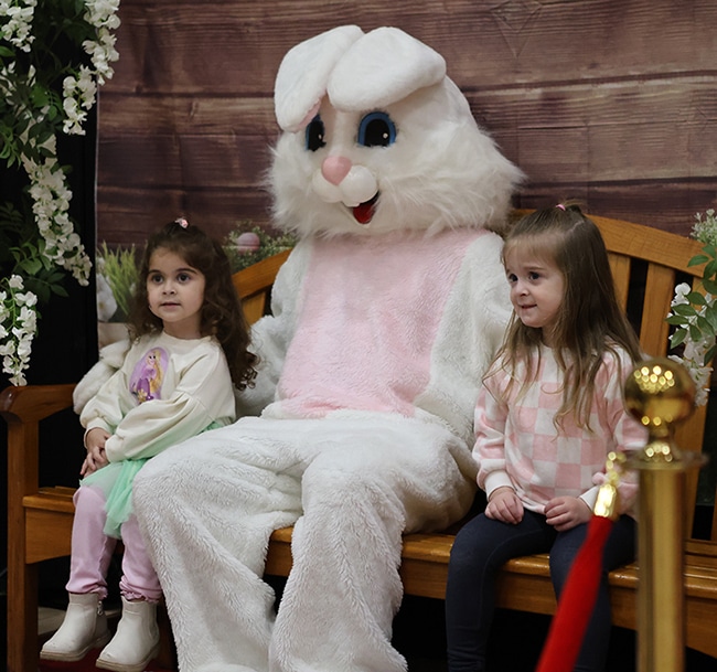 Two small girls sitting next to a volunteer in an Easter Bunny costume